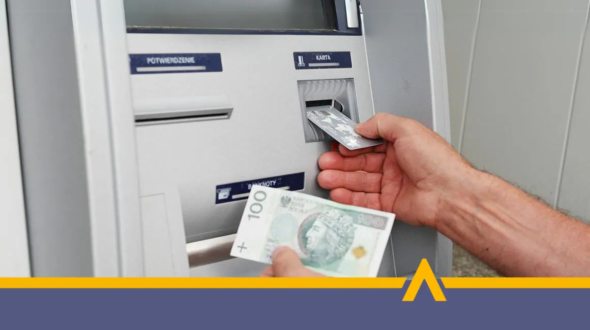 Osoba wypłacająca gotówkę z bankomatu – karta płatnicza i banknot 100 złotych