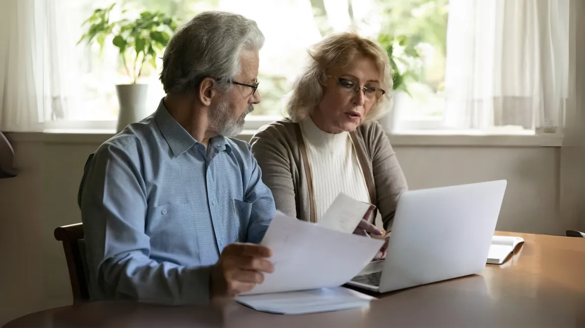 Starsze małżeństwo przeglądające dokumenty przy laptopie